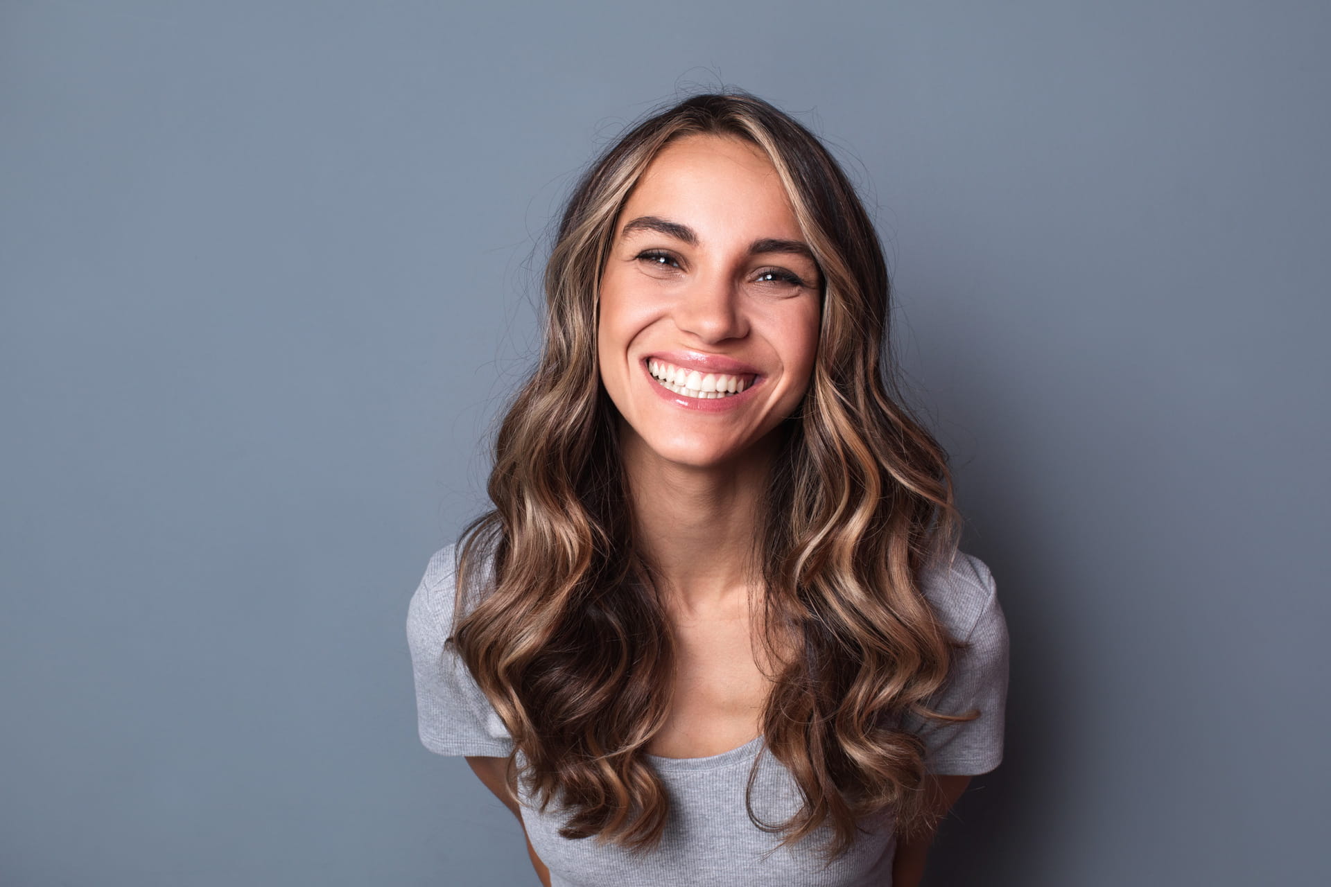 Smiling young woman with long wavy hair on a grey background