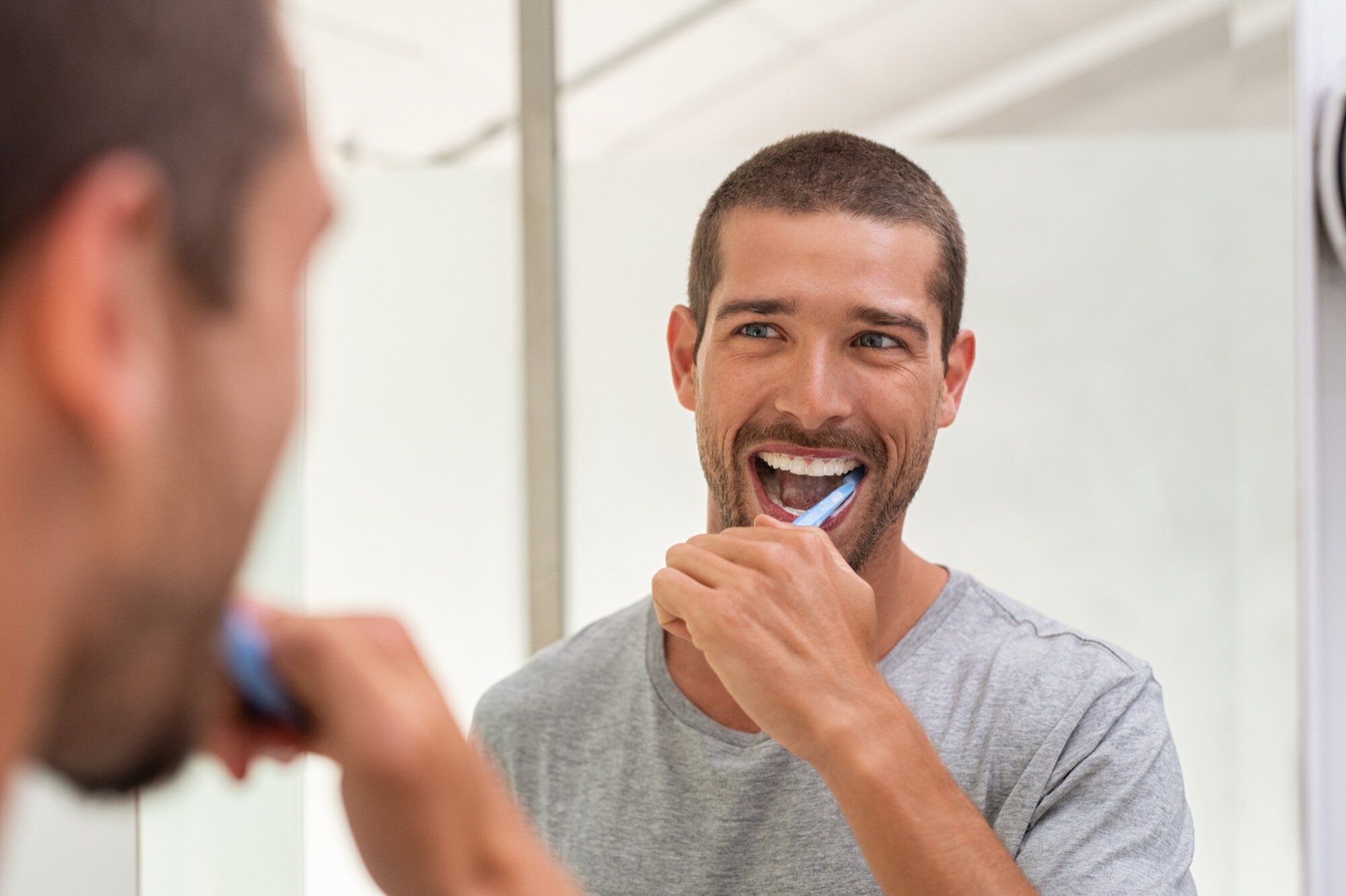 Man brushing his teeth at the bathroom mirror as part of a daily oral hygiene routine